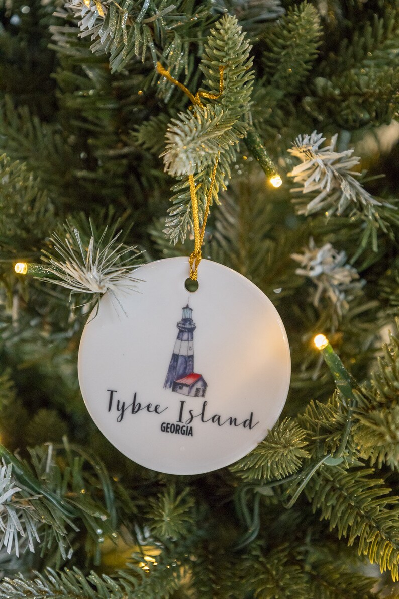 Puede incluir: Adorno navide&ntilde;o de cer&aacute;mica blanca con una ilustraci&oacute;n de un faro y el texto "Tybee Island, Georgia".