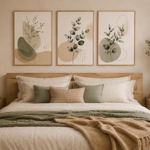 Puede incluir: Tres cuadros de pared con ilustraciones botánicas de hojas y tallos con formas abstractas en tonos verde y beige, dispuestos en fila sobre una cama con ropa de cama en capas en colores neutros y verde salvia a juego.