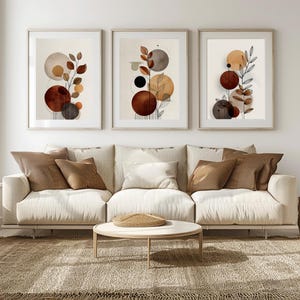 Könnte beinhalten: Drei gerahmte Kunstdrucke mit abstrakten botanischen Designs. Die Drucke zeigen braune, orange und graue kreisförmige Formen und blattartige Elemente. Sie hängen über einem cremefarbenen Sofa mit braunen Kissen, einem runden Couchtisch und einem strukturierten Teppich.