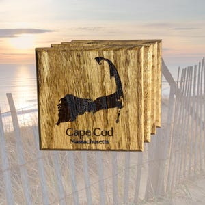 May include: Set of four wooden coasters featuring a burnt-in design of Cape Cod, Massachusetts. The coasters are a dark brown color with a natural wood grain.