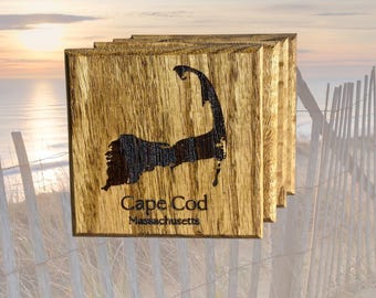 May include: Set of four wooden coasters featuring a burnt-in design of Cape Cod, Massachusetts. The coasters are a dark brown color with a natural wood grain.