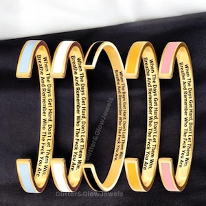 Puede incluir: Brazaletes de metal dorado con detalles de esmalte en azul claro, blanco, negro, amarillo y rosa. Cada brazalete tiene el texto grabado: "When The Days Get Hard, Don't Let Them Win. Breathe And Remember Who The F*ck You Are."