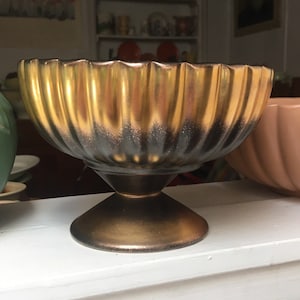 May include: A gold and black ceramic planter with a fluted design and a pedestal base.