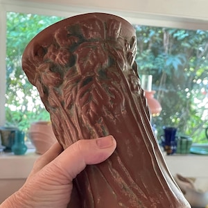 May include: A brown ceramic vase with a textured surface and a floral design. The vase is hand-painted with a green glaze.