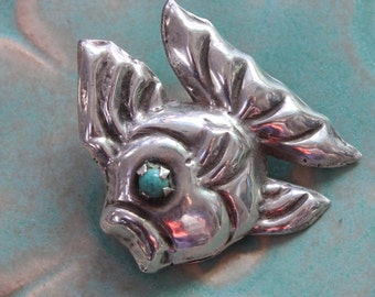 May include: A silver fish brooch with a turquoise stone eye.