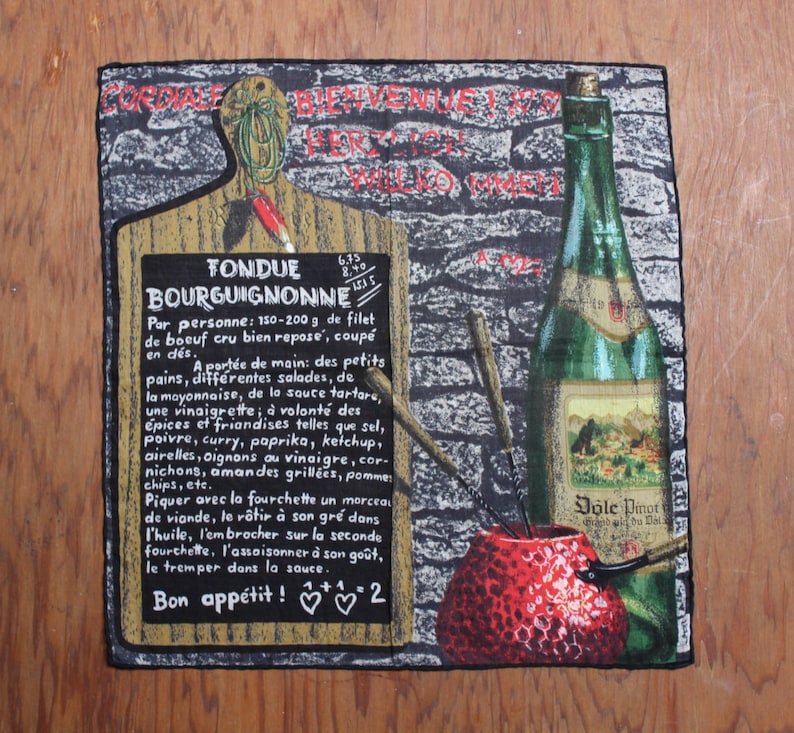 May include: A black and white tapestry depicting a fondue set with a red pot, a bottle of wine, and a wooden cutting board with the text "Fondue Bourguignonne" and instructions for preparing the dish. The tapestry also features a red apple and a brick wall background.
