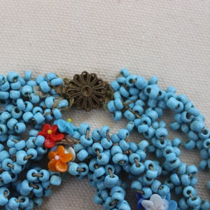 May include: A multi-strand necklace made of turquoise blue beads with colorful flower accents and a gold-toned clasp.