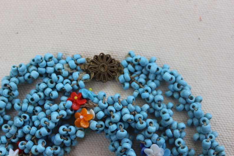 May include: A multi-strand necklace made of turquoise blue beads with colorful flower accents and a gold-toned clasp.