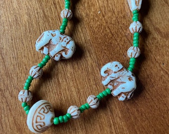 May include: A white and green beaded necklace with white elephant charms. The beads are small and round, and the elephant charms are detailed with intricate carvings.