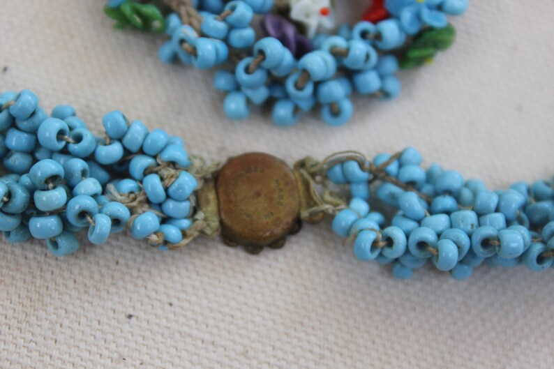 May include: A blue beaded necklace with a brass clasp. The necklace is made of multiple strands of small, round beads.