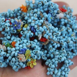 May include: A strand of blue glass beads with colorful flower accents. The beads are strung on a thin thread and are perfect for making jewelry or crafts.