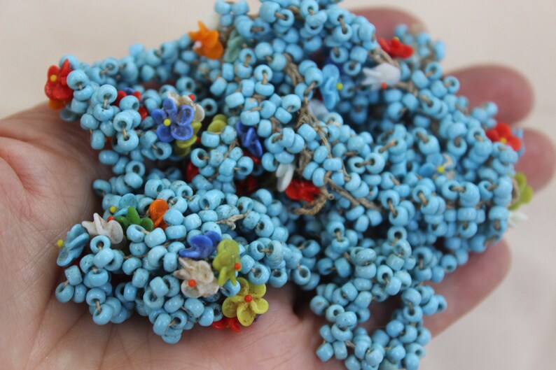 May include: A strand of blue glass beads with colorful flower accents. The beads are strung on a thin thread and are perfect for making jewelry or crafts.