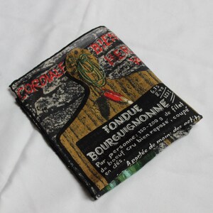 May include: A black and brown fabric pouch with a vintage design featuring a fondue recipe. The text reads "Fondue Bourguignonne" and includes instructions for preparing the dish. The pouch is folded and has a green and white striped border.