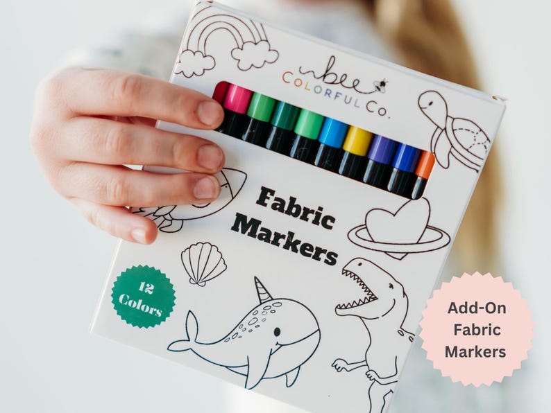 Close-up image of a girl holding Bee Colorful Co. fabric markers. Includes graphic 'Add-On Fabric Markers'.