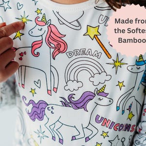 Close-up of unicorn coloring pajamas with 'Made from Softest Bamboo' graphic. Girl points to a colorful design she created.