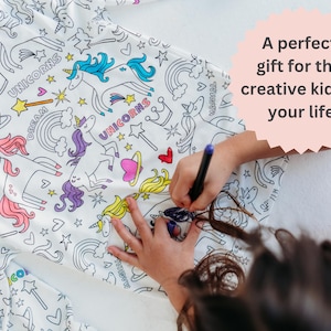 Image shows a young girl joyfully coloring her unicorn pajamas with vibrant fabric markers. The photo includes the text 'A perfect gift for the creative kids in your life,' highlighting the imaginative play and personalized gift aspect of these pajamas.
