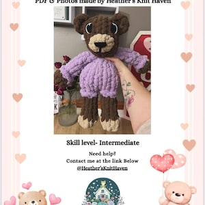 May include: A handmade crochet bear with a brown head, tan snout, and light purple body. The bear is wearing a light purple sweater and brown shorts. The text "The Huggable Heart Bear" is at the top of the image. The skill level is intermediate.