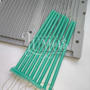 May include: A set of teal-colored taper candles with wicks, resting on a gray candle mold. The candles are grouped together, ready for use. The image includes the text "ETERNAL LUMOS".