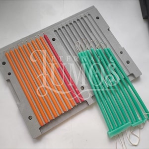 May include: A close-up shot of a candle-making mold with several orange, red, and green candles. The candles are long and thin, and they are arranged in rows within the mold. The mold is gray and has a rectangular shape. The text "ETERNAL MOS" is visible.
