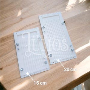 May include: Two white rectangular objects with a ridged surface, secured with screws. One measures 15 cm, the other 20 cm. The text "ETERNAL LUMOS" is visible on the objects. They are placed on a wooden surface.