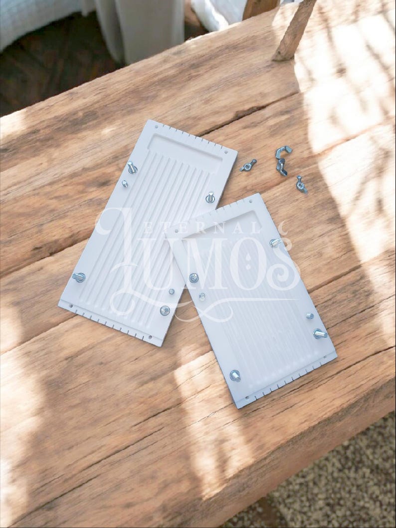 May include: Two white rectangular objects with parallel grooves and metal hardware are displayed on a wooden surface. Several loose screws and bolts are scattered nearby. The objects appear to be components of a larger item.