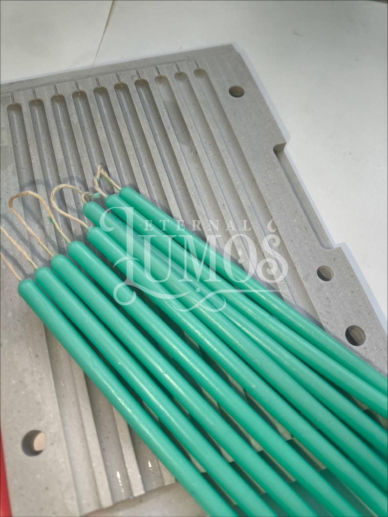 May include: A collection of teal-colored taper candles with wicks, resting on a gray candle mold. The candles are cylindrical and have a smooth finish. The mold has multiple slots for candle creation. The image includes the text "ETERNAL LUMOS".