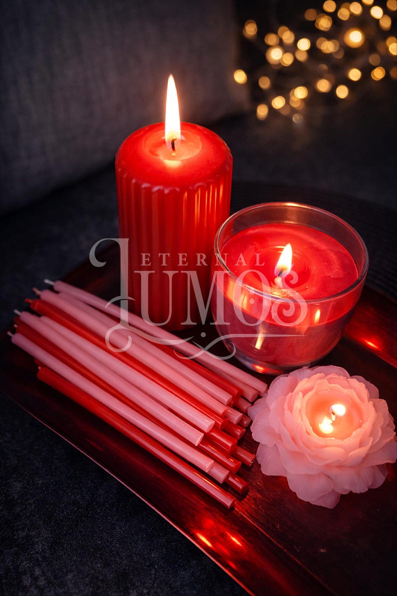 May include: A collection of lit candles in various shapes and sizes, including a large red pillar candle, a glass-encased candle, and a flower-shaped candle. Several red and pink taper candles are arranged on a red tray. The image includes the text "ETERNAL UMO".