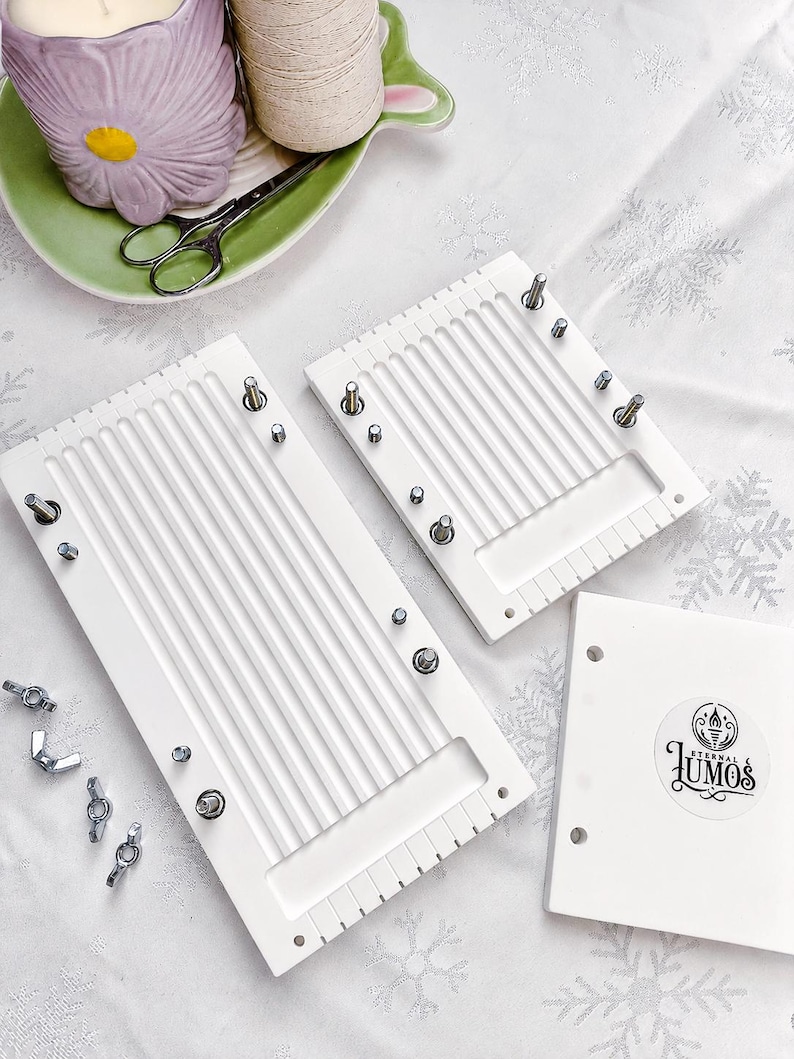 May include: White weaving loom set with metal hardware, including wing nuts and screws. The set includes two rectangular looms, a small square piece with a logo, and additional hardware. The looms have vertical grooves and are designed for weaving projects.