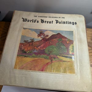 May include: A vintage book titled "The Standard Treasury of the World's Great Paintings." The cover features a colorful landscape painting with palm trees, a mountain, and a path. The book has a beige cover.