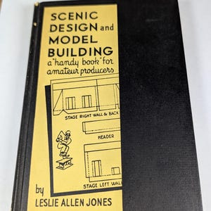 May include: A vintage book titled "SCENIC DESIGN and MODEL BUILDING" with a black cover and a yellow rectangular label. The label features text and illustrations, including stage diagrams. The author's name, Leslie Allen Jones, is also visible.