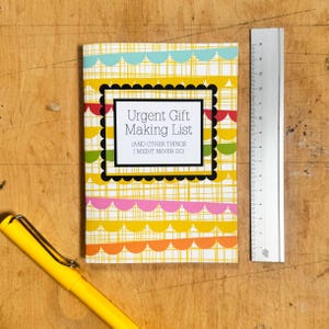 May include: A yellow, green, red, and blue patterned notebook with the text "Urgent Gift Making List (and other things I might never do)" on the front cover.
