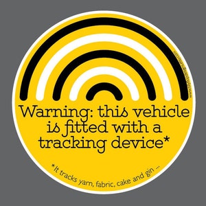 May include: A yellow circle with black and white stripes, resembling a rainbow, and the text "Warning: this vehicle is fitted with a tracking device* *It tracks yarn, fabric, cake and gin..."
