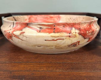 May include: A wooden bowl with a natural wood finish and red and orange swirls. The bowl has a unique, organic shape and is perfect for serving snacks or fruit.