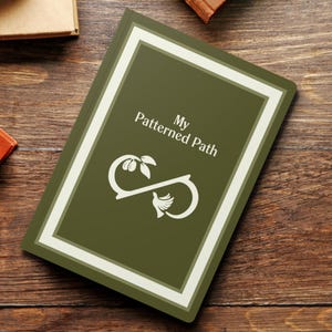 May include: A hardcover journal with a green cover and a white border. The cover features the text "My Patterned Path" and a white graphic of an infinity symbol with olive branches and a dove. The journal is on a wooden surface.