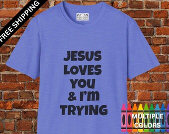 May include: A periwinkle blue t-shirt with the text "JESUS LOVES YOU & I'M TRYING" in black. The shirt has a crew neck and short sleeves. The words "MULTIPLE COLORS" are displayed with a crayon graphic.