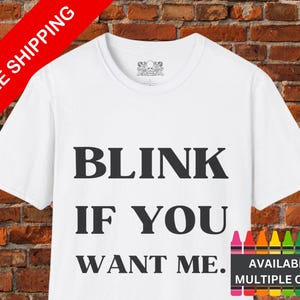May include: White t-shirt with black text that reads "Blink if you want me."  The text is in a bold, sans-serif font.  The shirt is available in multiple colors.