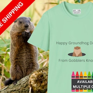 May include: A light green t-shirt with the text "Happy Groundhog Day! From Gobblers Knob" and a cartoon groundhog in a hole. The shirt is available in multiple colors, as shown by the row of colored crayons at the bottom.