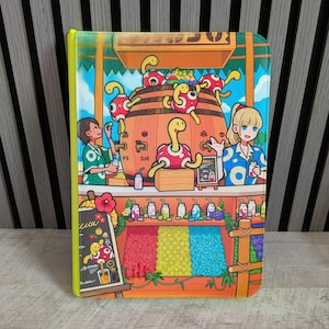 Pode incluir: Uma capa retangular para tablet com uma ilustração vibrante de uma banca de sumos tropical. A cena mostra duas pessoas a servir bebidas de um grande barril de madeira rodeado por criaturas amarelas e vermelhas semelhantes a tartarugas. Abaixo, prateleiras exibem frutas coloridas e garrafas.