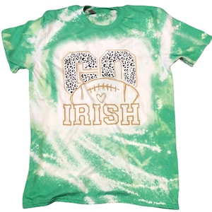 K&ouml;nnte beinhalten: Gr&uuml;n-wei&szlig;es Batik-T-Shirt mit einer goldenen Grafik eines Fu&szlig;balls mit den Worten "Go Irish" in einem Leopardenmuster.