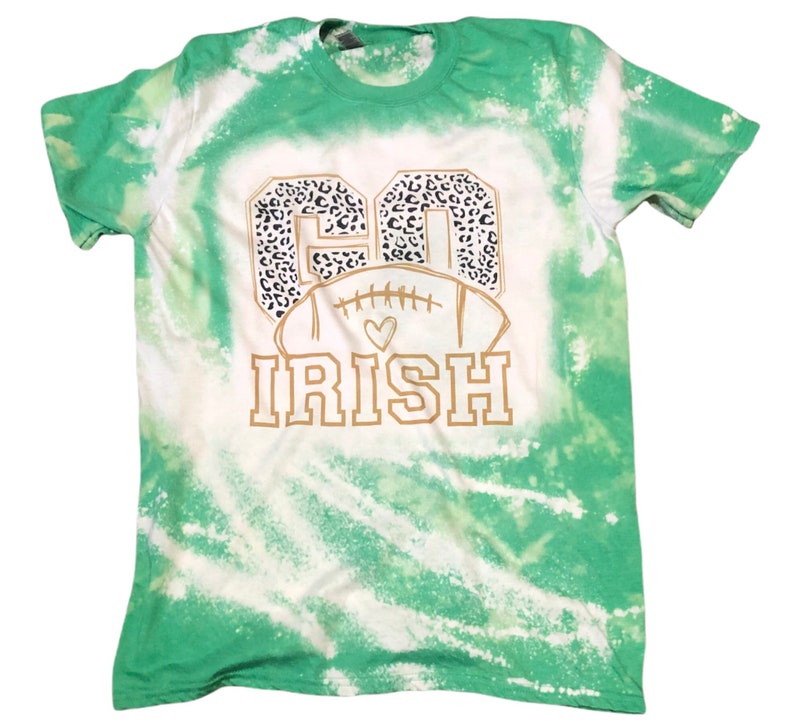 K&ouml;nnte beinhalten: Gr&uuml;n-wei&szlig;es Batik-T-Shirt mit einer goldenen Grafik eines Fu&szlig;balls mit den Worten "Go Irish" in einem Leopardenmuster.