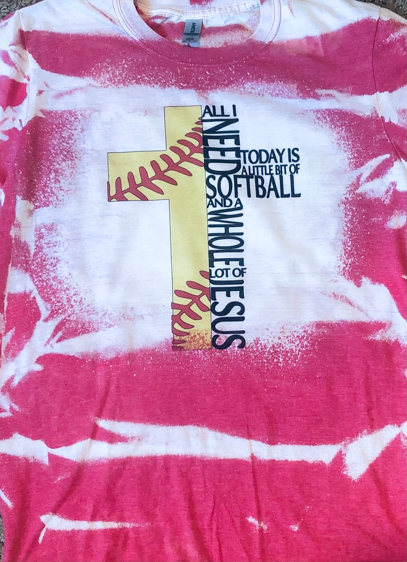 May include: A red and white tie-dye t-shirt with a yellow baseball cross design. The text on the shirt reads "All I Need is a little bit of Softball and a Whole Lot of Jesus".