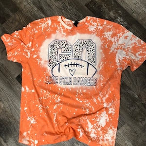 K&ouml;nnte beinhalten: Orangefarbenes, gebleichtes T-Shirt mit einem wei&szlig;en und schwarzen Leopardenmuster-Fu&szlig;ball-Design. Der Text "Lone Star Rangers" ist unter dem Fu&szlig;ball gedruckt.