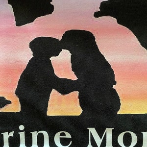 Peut inclure: T-shirt noir avec une silhouette de deux personnes qui s'embrassent devant un coucher de soleil rose, orange et jaune. Le texte "Marine Mom" est imprim&eacute; sous la silhouette.