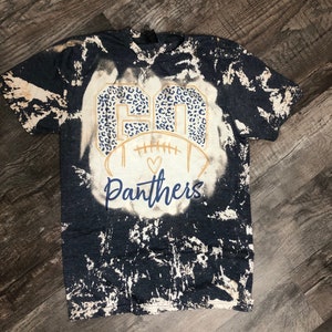 K&ouml;nnte beinhalten: Ein schwarz-wei&szlig;es Batik-T-Shirt mit einer goldenen Football-Grafik und dem Text "GO Panthers" in einem Leopardenmuster.