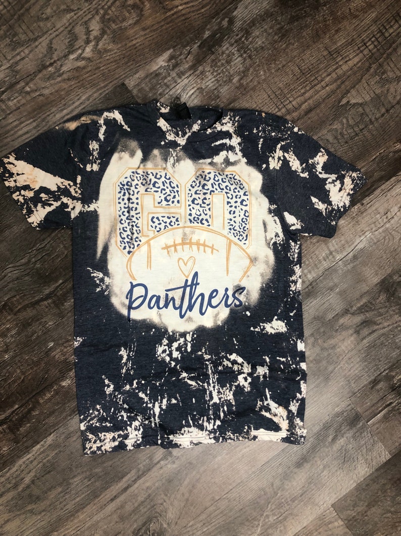K&ouml;nnte beinhalten: Ein schwarz-wei&szlig;es Batik-T-Shirt mit einer goldenen Football-Grafik und dem Text "GO Panthers" in einem Leopardenmuster.