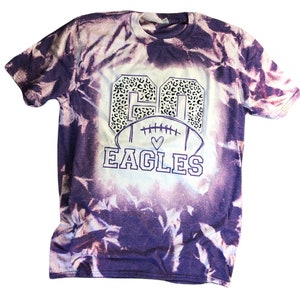 K&ouml;nnte beinhalten: Lilafarbenes Batik-T-Shirt mit einer wei&szlig;en Football-Grafik und dem Text "GO EAGLES" in wei&szlig;er Umrandung. Die Nummer "60" befindet sich in der Football-Grafik mit einem Leopardenmuster.