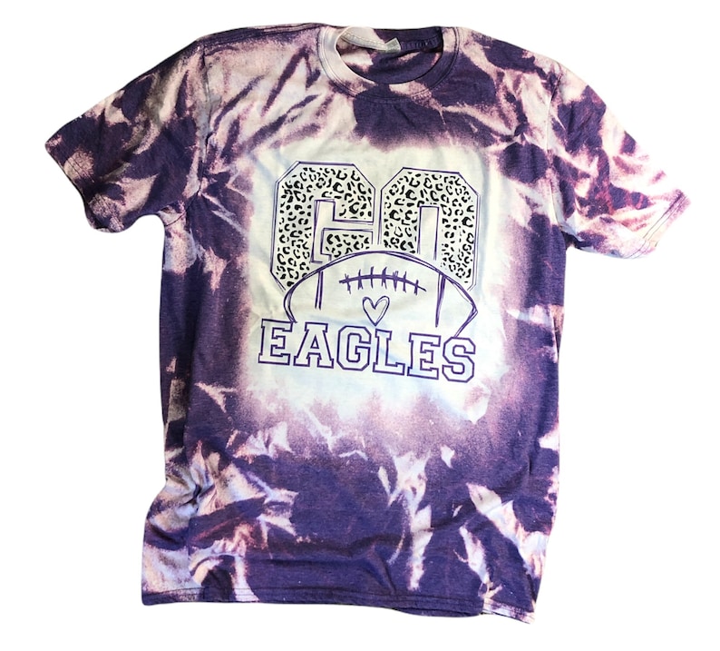 K&ouml;nnte beinhalten: Lilafarbenes Batik-T-Shirt mit einer wei&szlig;en Football-Grafik und dem Text "GO EAGLES" in wei&szlig;er Umrandung. Die Nummer "60" befindet sich in der Football-Grafik mit einem Leopardenmuster.