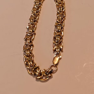 May include: A gold chain bracelet with a Byzantine style design. The bracelet has a clasp closure.