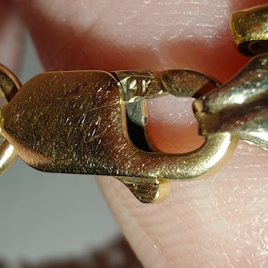 May include: Close-up of a gold chain with a clasp. The clasp has a marking that reads "14K".