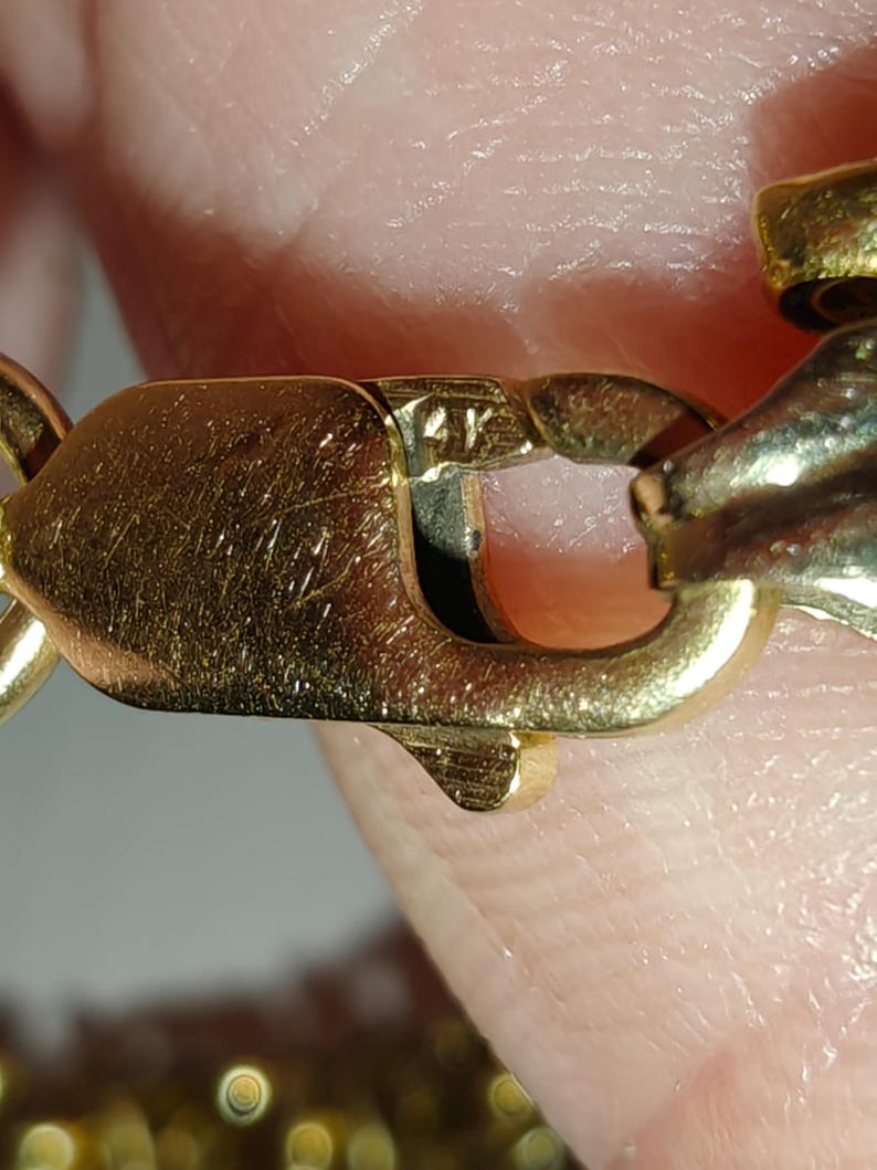 May include: Close-up of a gold chain with a clasp. The clasp has a marking that reads "14K".